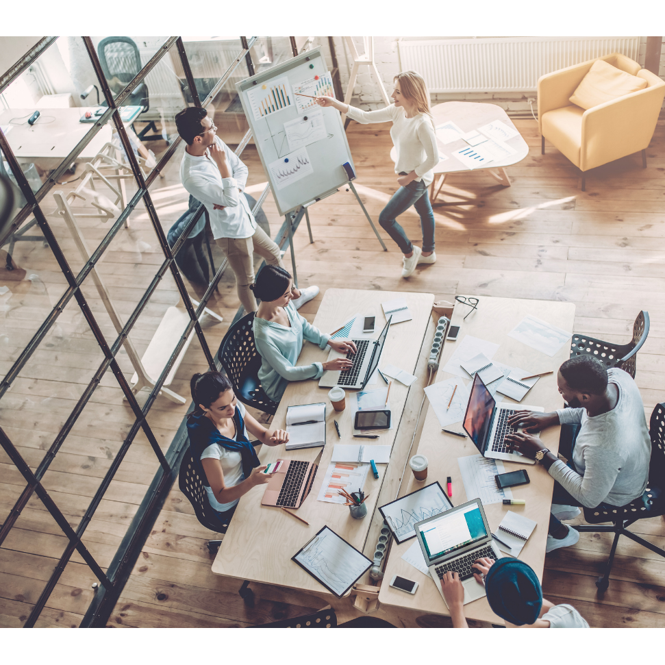 Gruppendiskussion am Tisch mit Laptops, Notizen und einem Präsentationsboard im Hintergrund.