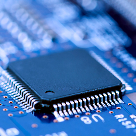 Schwarzer Mikrochip auf einer blauen Leiterplatte mit feinen Leiterbahnen.