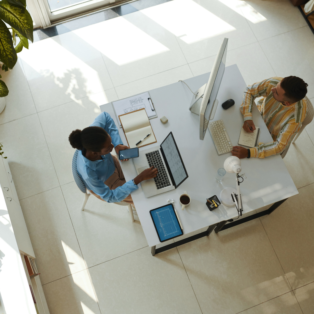 Zwei Personen sitzen an einem Tisch, arbeiten an einem Laptop und haben Dokumente vor sich.