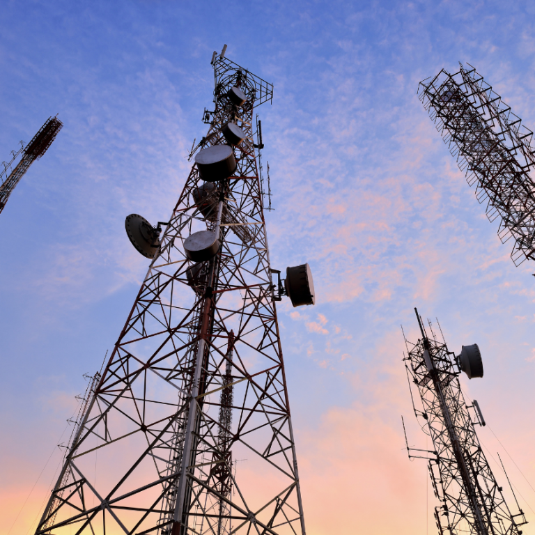 Hohe Mobilfunkmasten gegen einen bunten Himmel bei Sonnenuntergang.
