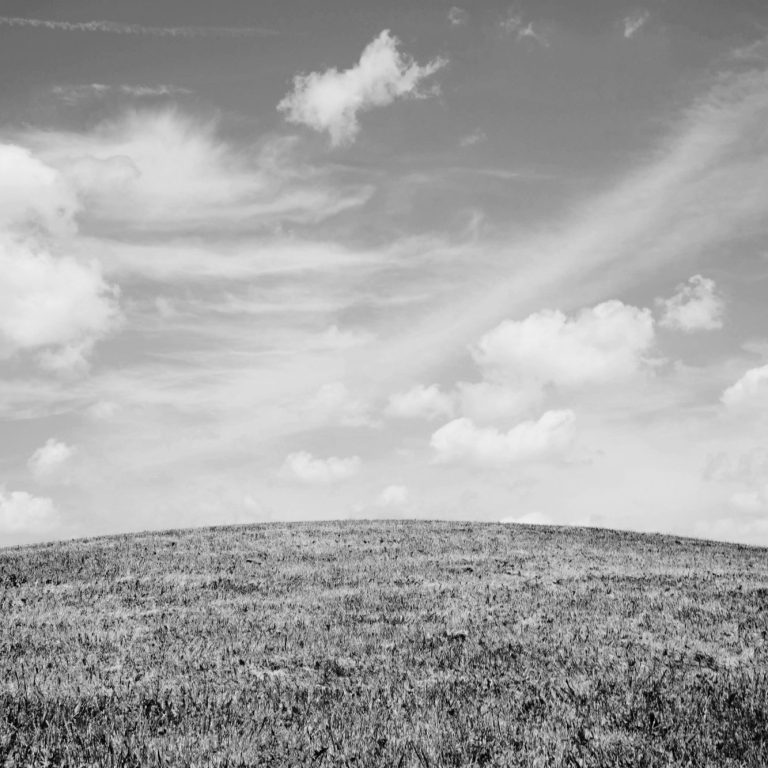 Schwarze und weiße Landschaft mit hügeliger Erde und bewölktem Himmel.