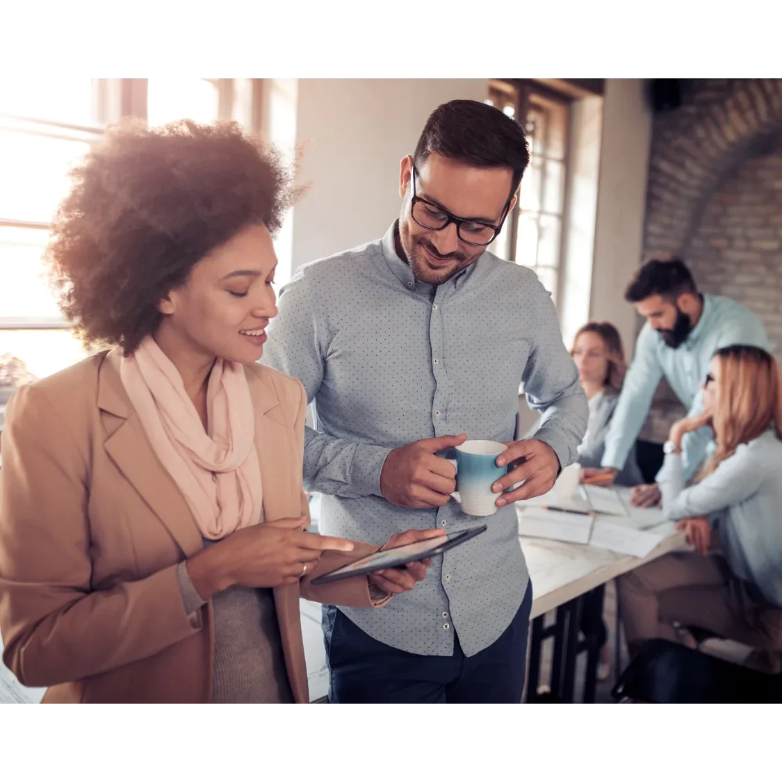 Zwei Personen besprechen eine digitale Präsentation, während andere im Hintergrund arbeiten.